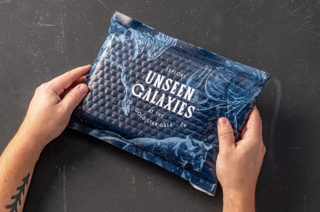 Hands holding the outer packaging of the 2024 Monroe County Community College Foundation Gold Star Gala invitation